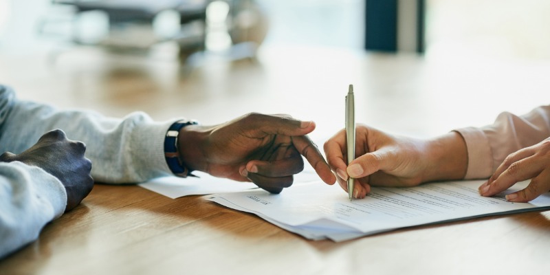 Person signing a contract while someone else shows them where to sign