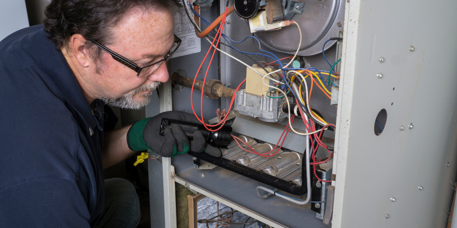 Tech looking at furnace - 6 HVAC Fall Maintenance Tips According to the Experts