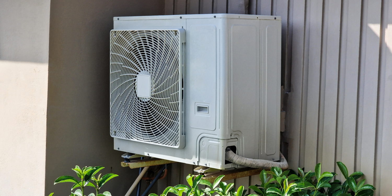 Older Heat pump outside of home surrounded by plants - Understanding Heat Pumps: An FAQ Guide for Canadian Homeowners